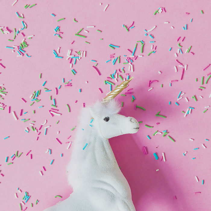A white unicorn with a Golden horn and confetti on pink background.