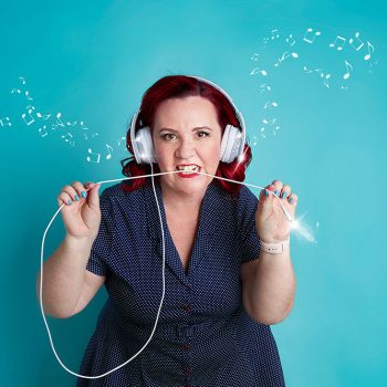 brand portrait of a tech expert against a teal background wearing earphones and biting the cable