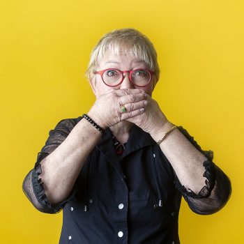 brand portrait of speaker with yellow background and covering her mouth with her hands